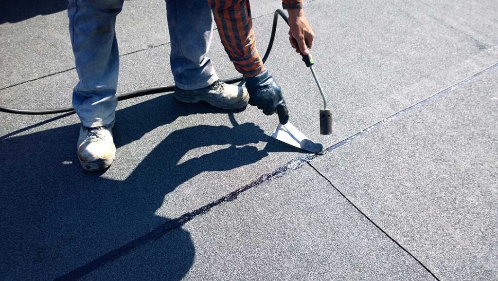 Worker secures a temporary tarp over a damaged roof while a homeowner observes from the ground.