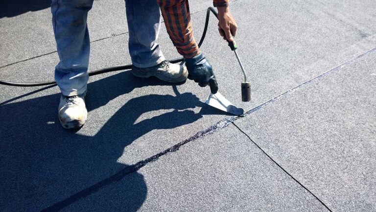 Worker secures a temporary tarp over a damaged roof while a homeowner observes from the ground.